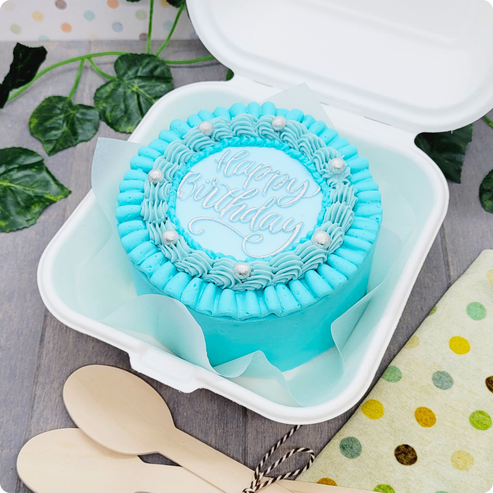Blauwe bento cake met zilveren Happy Birthday tekst en eetbare parels in open verpakking

