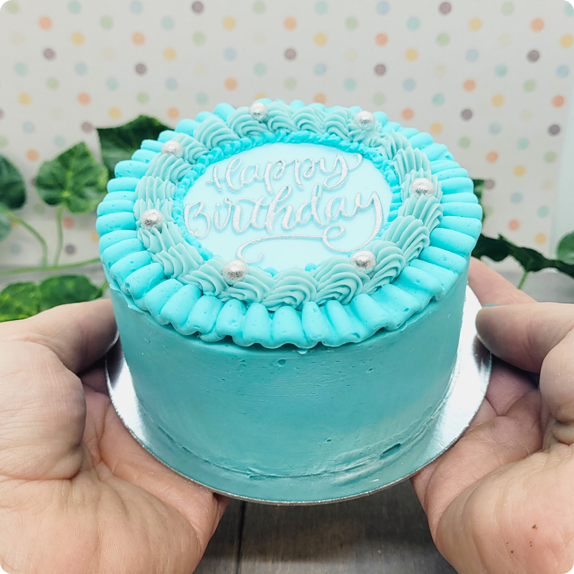 Blauw mini taartje met blauwe ruffles en zilveren tekst, gepresenteerd in handen