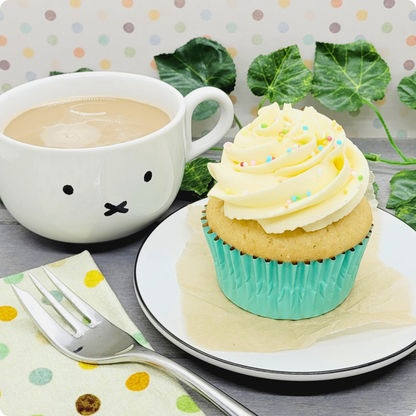 Vegan vanillecupcake geserveerd op een bord met een kop koffie, perfect voor een plantaardige zoete pauze.