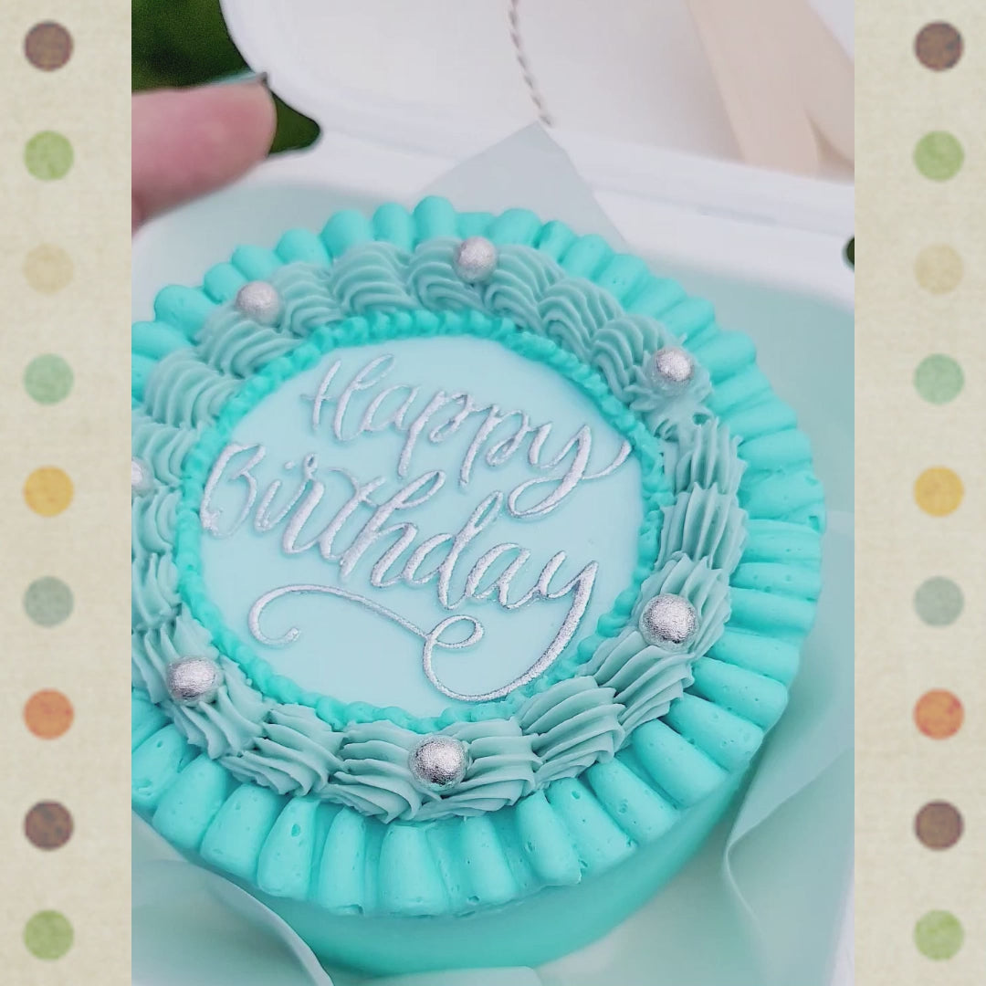 Bento cake in open bio verpakking, met blauwe ruffles en zilveren decoratie, vastgehouden buiten